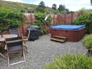 Un jardin avec un jacuzzi, un barbecue couvert et une table avec des chaises.