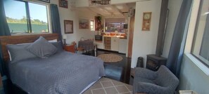 Une chambre à coucher avec un lit, une chaise, une petite table, une fenêtre et, au fond, un coin cuisine.