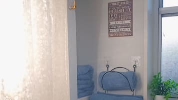 Ein Badezimmer mit Duschvorhang, Hinweisschild für die Toilette, Handtüchern an Haken, einer Topfpflanze und einem Fenster.