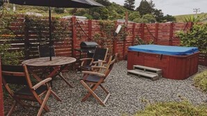 A patio area with a round table and two chairs, a barbecue grill, and a hot tub.