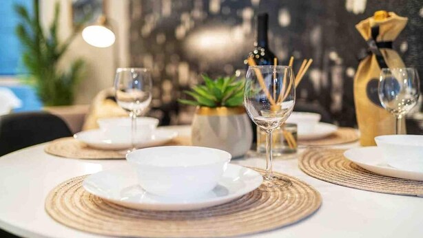A dining table set with white plates, bowls, and glasses, with a bottle of wine and a candle in the center. - ⚡️ROOFTOP VIEWS⚡️The Helix⚡️Central🚶🏻‍♂️Walker’s paradise (Seattle)