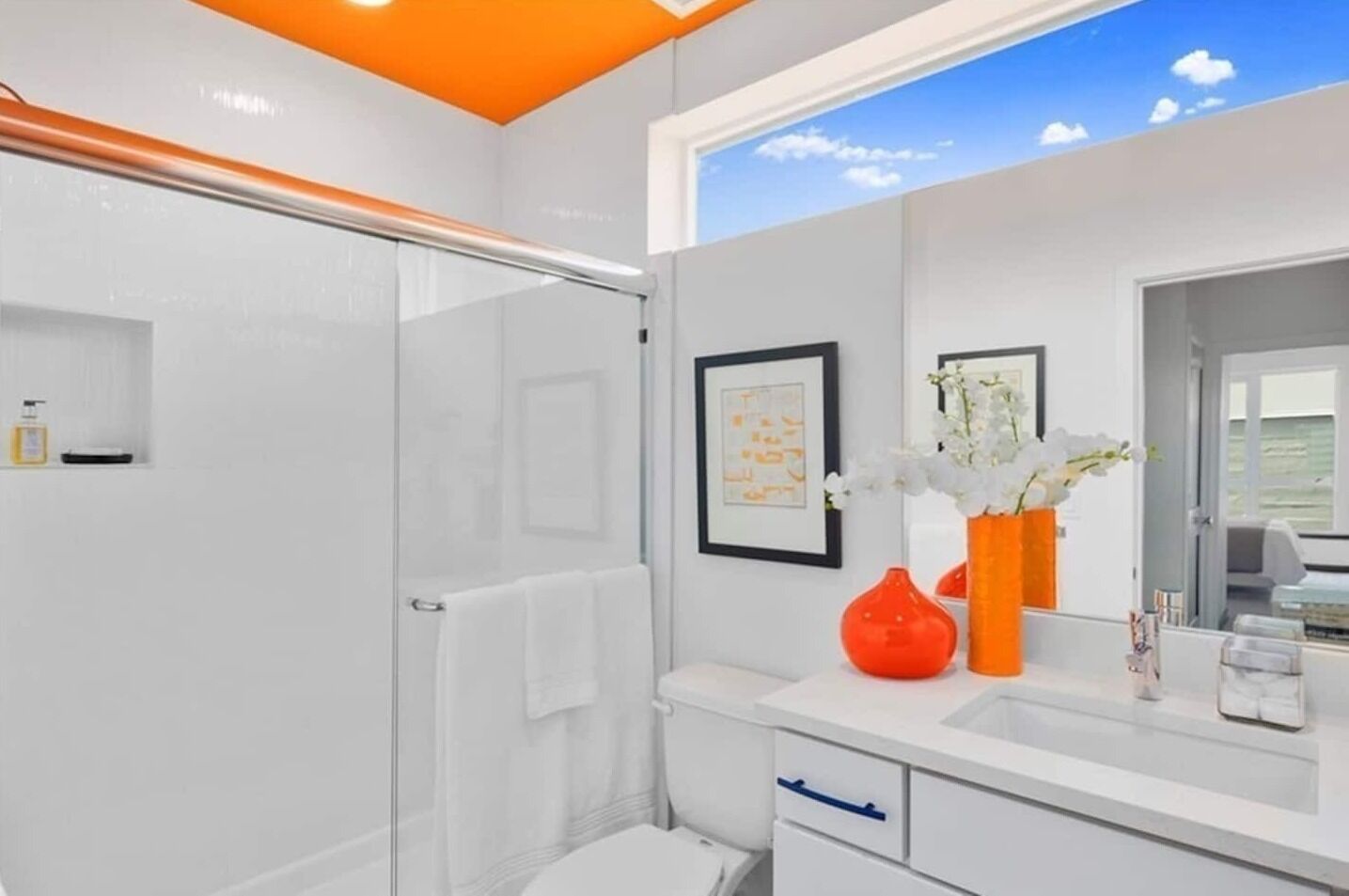 Un baño moderno con cabina de ducha de vidrio, un lavabo blanco con espejo y un jarrón con flores blancas.