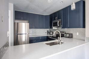 Una cocina moderna con armarios azul oscuro, electrodomésticos de acero inoxidable y encimera blanca.
