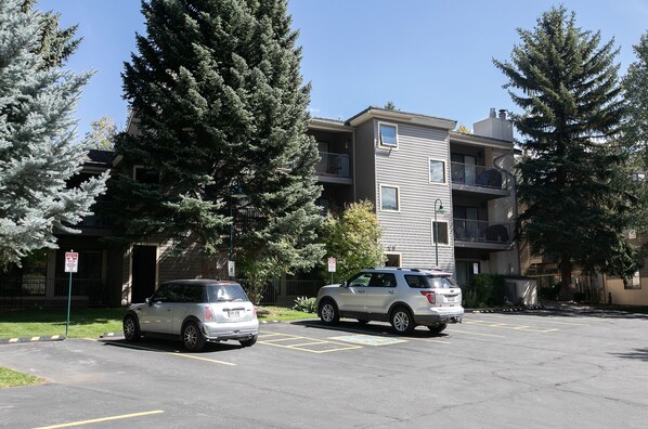 Un parking avec deux voitures, un immeuble doté de balcons et des arbres tout autour.