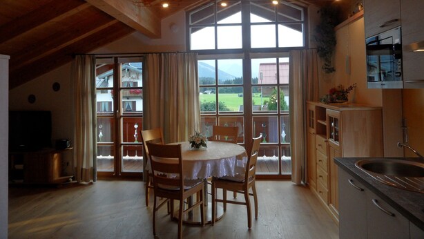 Ein Essbereich mit Tisch und Stühlen, eine Küche mit Spüle und Herd sowie große Fenster mit Blick auf eine grüne Landschaft.