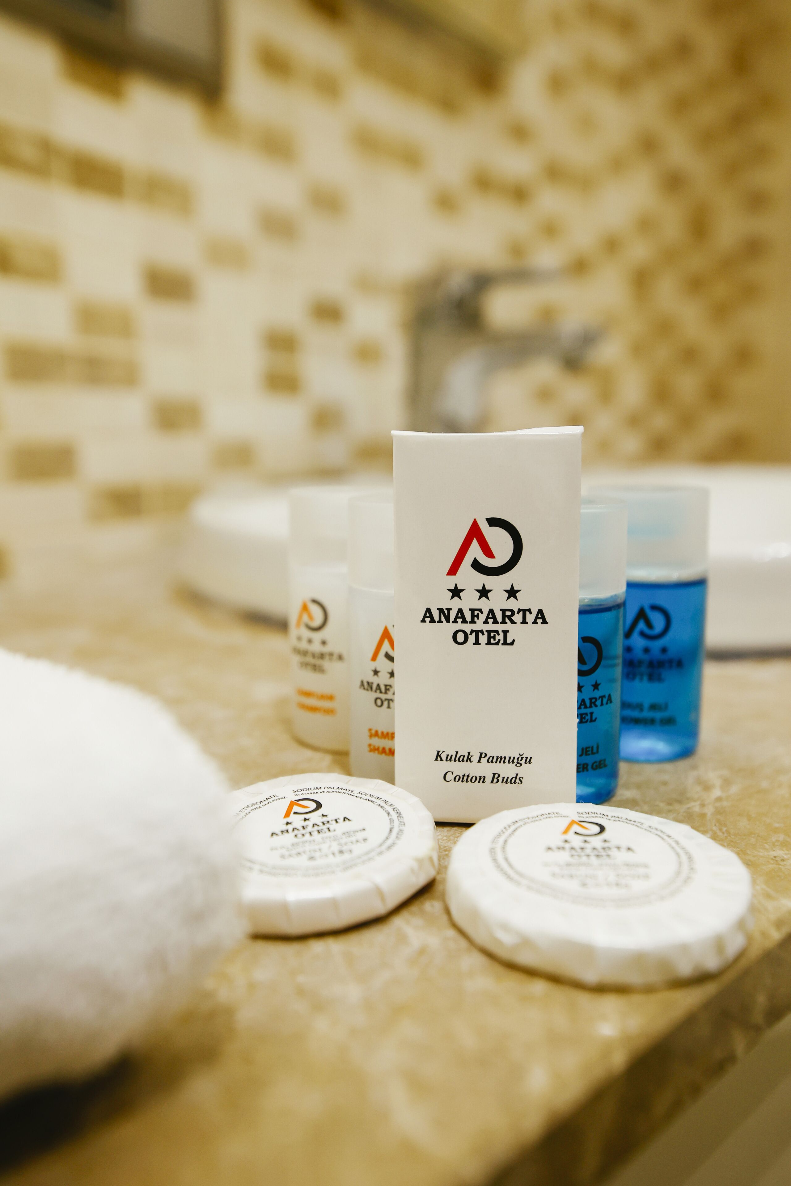 A bathroom counter with toiletries from Anafarta Hotel, including cotton bud cases and shampoo bottles.