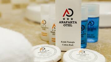 A bathroom counter with toiletries from Anafarta Hotel, including cotton bud cases and shampoo bottles.
