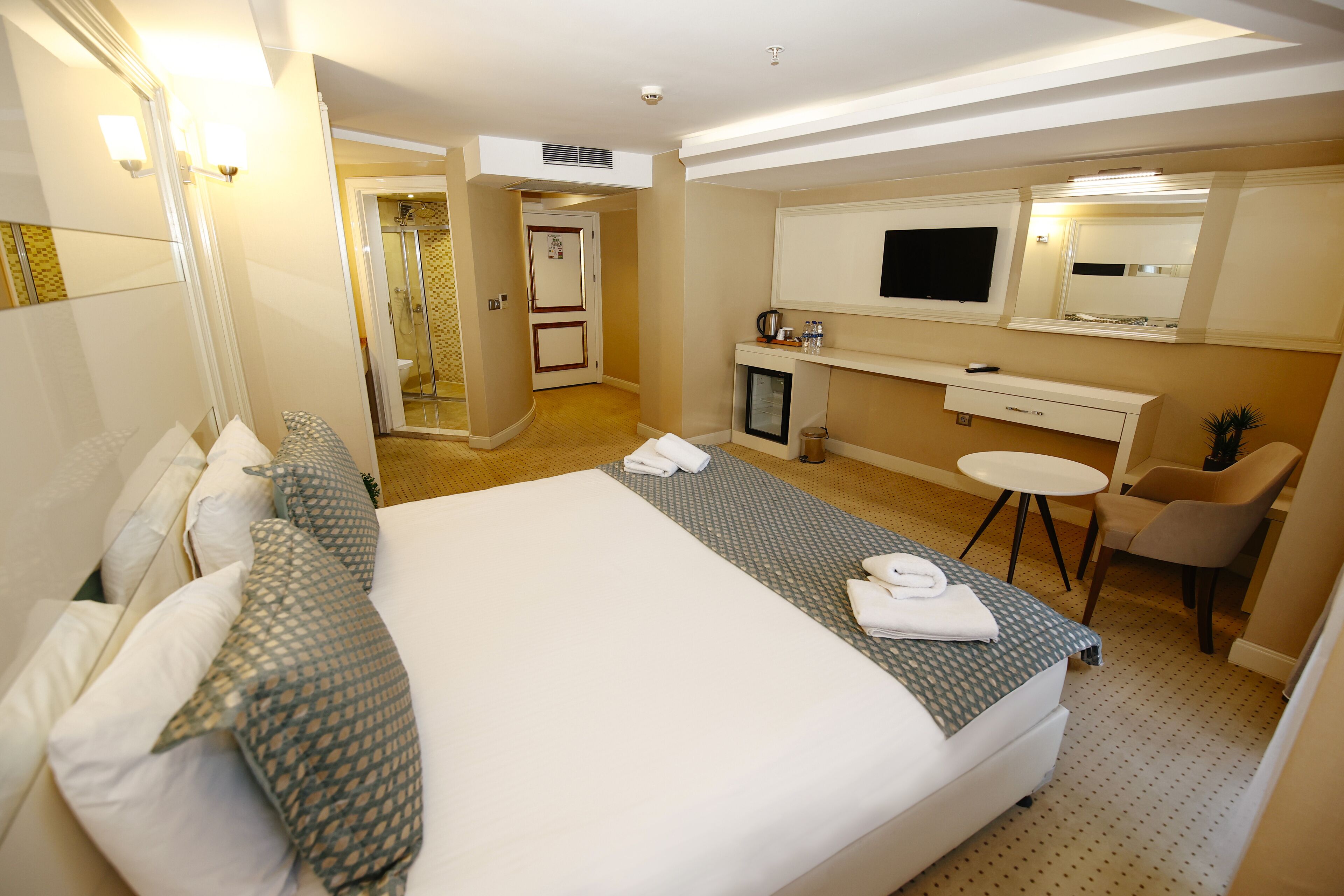 Une chambre d’hôtel avec un grand lit, un bureau avec un ordinateur, une télévision et un petit coin salon.