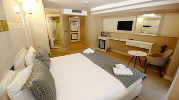 Une chambre d’hôtel avec un grand lit, un bureau avec un ordinateur, une télévision et un petit coin salon.