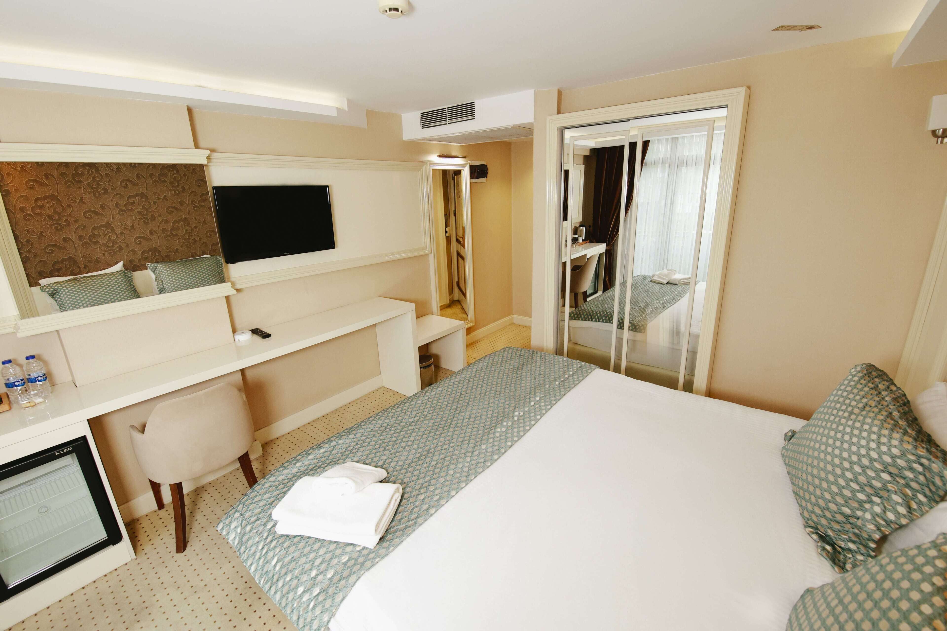 Habitación de hotel con cama, escritorio con ordenador, espejo y baño visible a través de una puerta abierta.