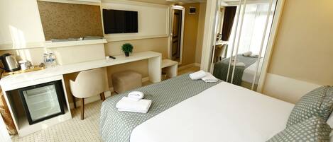 A hotel room with a bed, a desk, a television, a mirror, and a small refrigerator.
