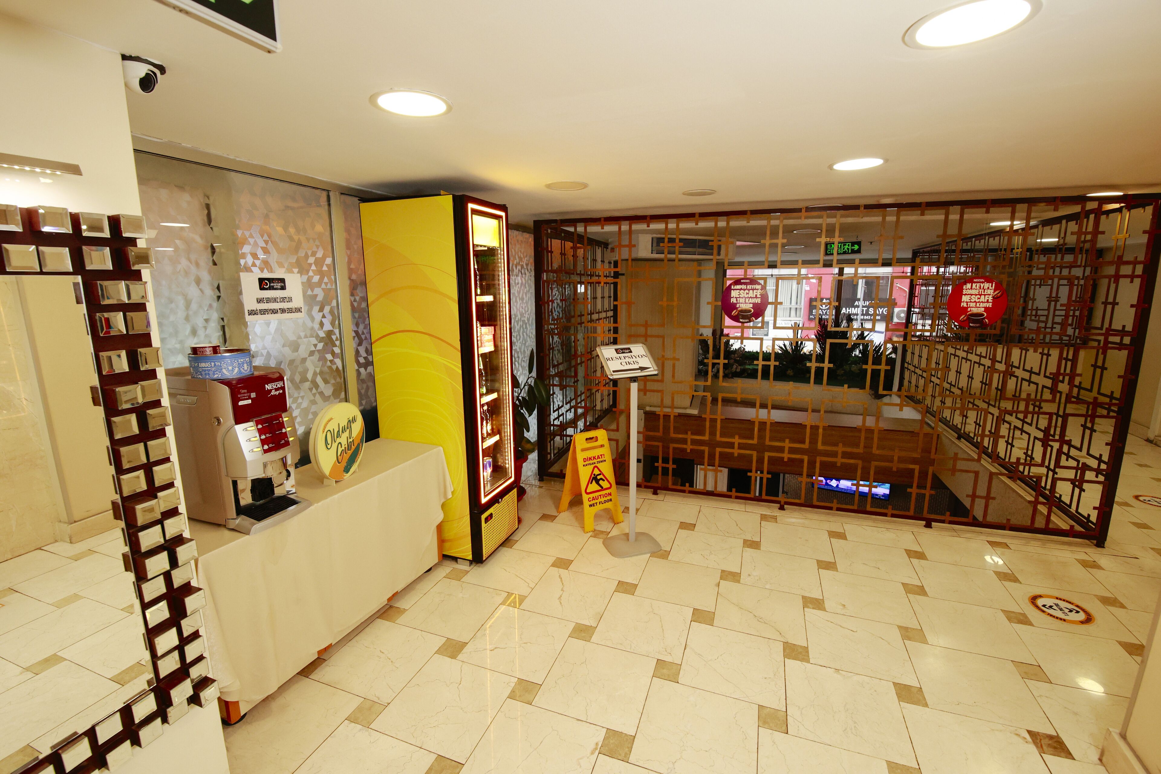 Un área de recepción con mostrador, máquina de café, cartel que indica zona para fumadores y cámara de seguridad.