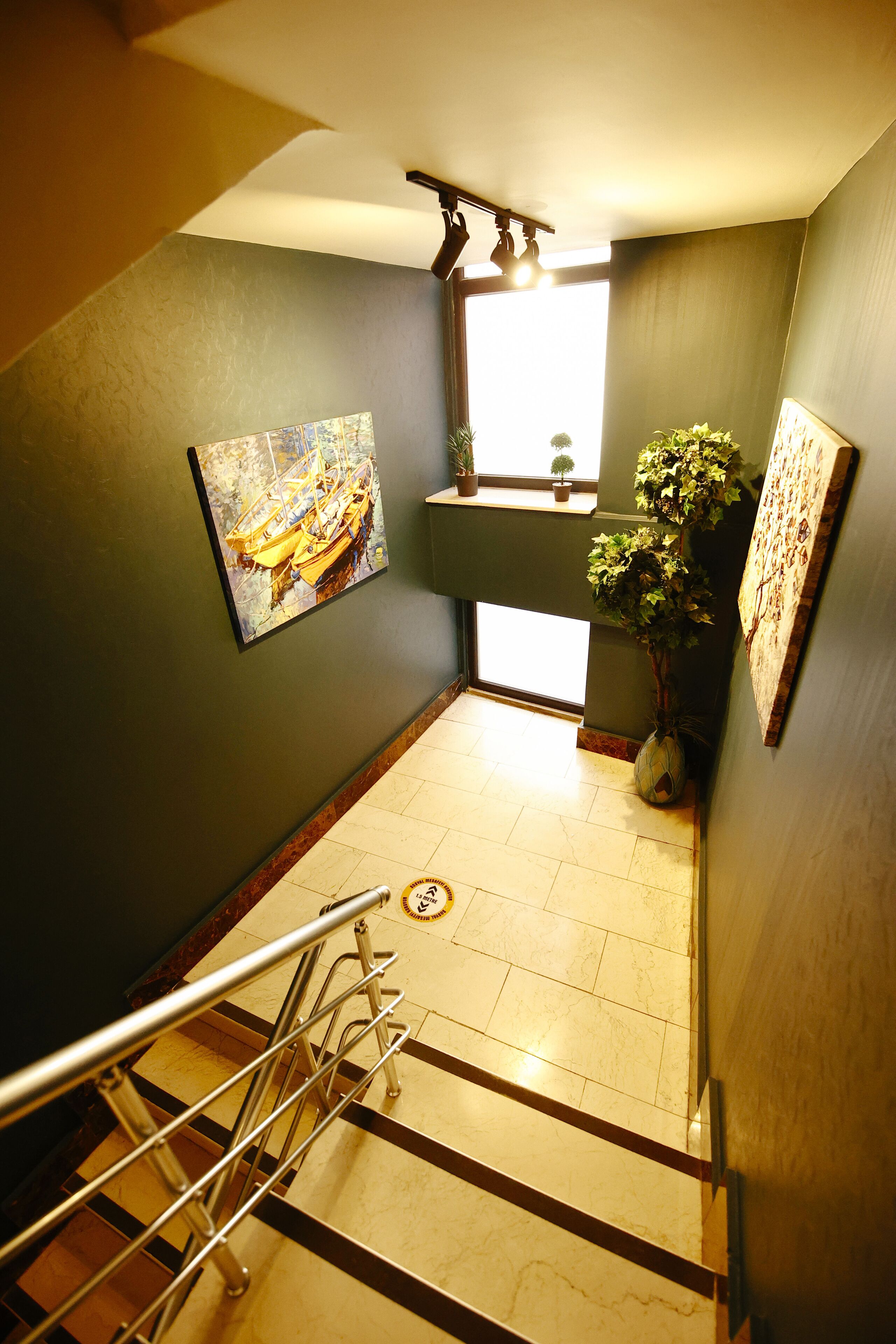 A hallway with a painting, a potted plant, and a window.