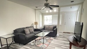 A living room with a black sofa, a glass coffee table, and a wooden chair. - 3 bedroom House in a quiet neighborhood (Orlando)