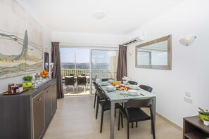 A dining area with a table set for two, a view of the cityscape through the balcony, and a painting on the wall.