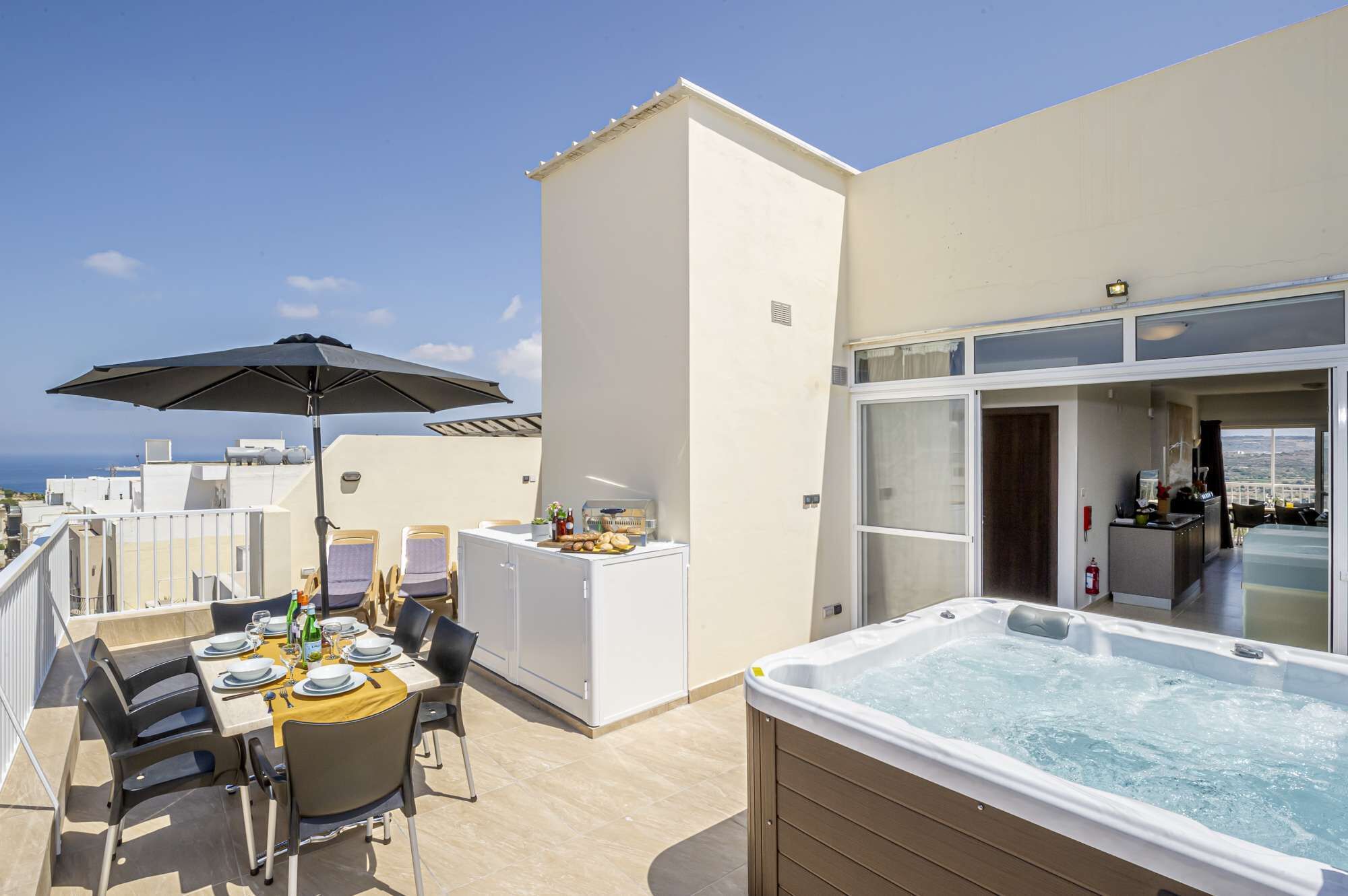 Una terrazza sul tetto con tavolo, sedie, vasca idromassaggio e area bar.