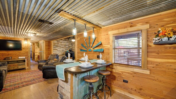 Interior rústico de una cabaña con barra de madera, asientos y chimenea de piedra.