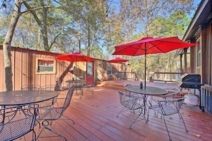 Una terraza de madera con mesas y sillas de metal, sombrillas rojas y una parrilla para barbacoa.