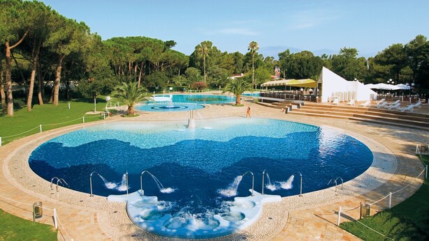 A large outdoor swimming pool with multiple water features, surrounded by a landscaped area with trees and a pavilion. - Relaxing Stay by the Sea (Baia Domizia (CE))