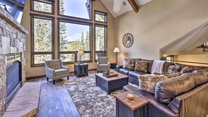 A spacious living room with a stone fireplace, large windows, a leather sofa, and a cozy rug. - 3 Fireplaces & Mtn View: Luxe Home in Breckenridge (Breckeridge)