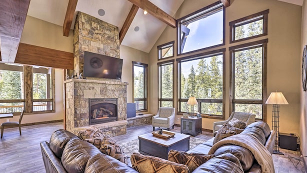 A spacious living room with a stone fireplace, leather sofas, and large windows offering a view of the forest. - 3 Fireplaces & Mtn View: Luxe Home in Breckenridge (Breckeridge)