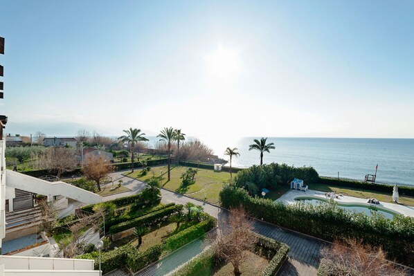 A residential area with a swimming pool, palm trees, and a view of the sea.