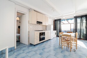 A modern kitchen with a dining area, featuring a large window with curtains, a built-in oven, and a washing machine.