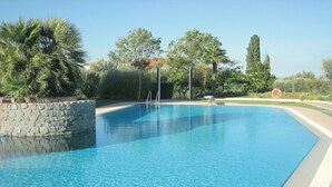 A clear swimming pool with stone walls, surrounded by greenery and trees.