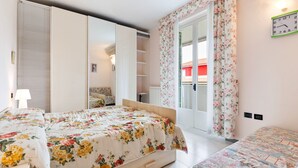 A bedroom with two beds, a wardrobe, a radiator, a clock, and a window with curtains.