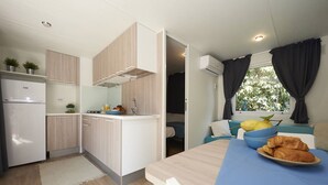 A compact kitchen with a refrigerator, sink, and cabinets, a dining area with a table and chairs, and a window with curtains. - Chalet w/ Terrace & Pool (Baia Domizia (CE))