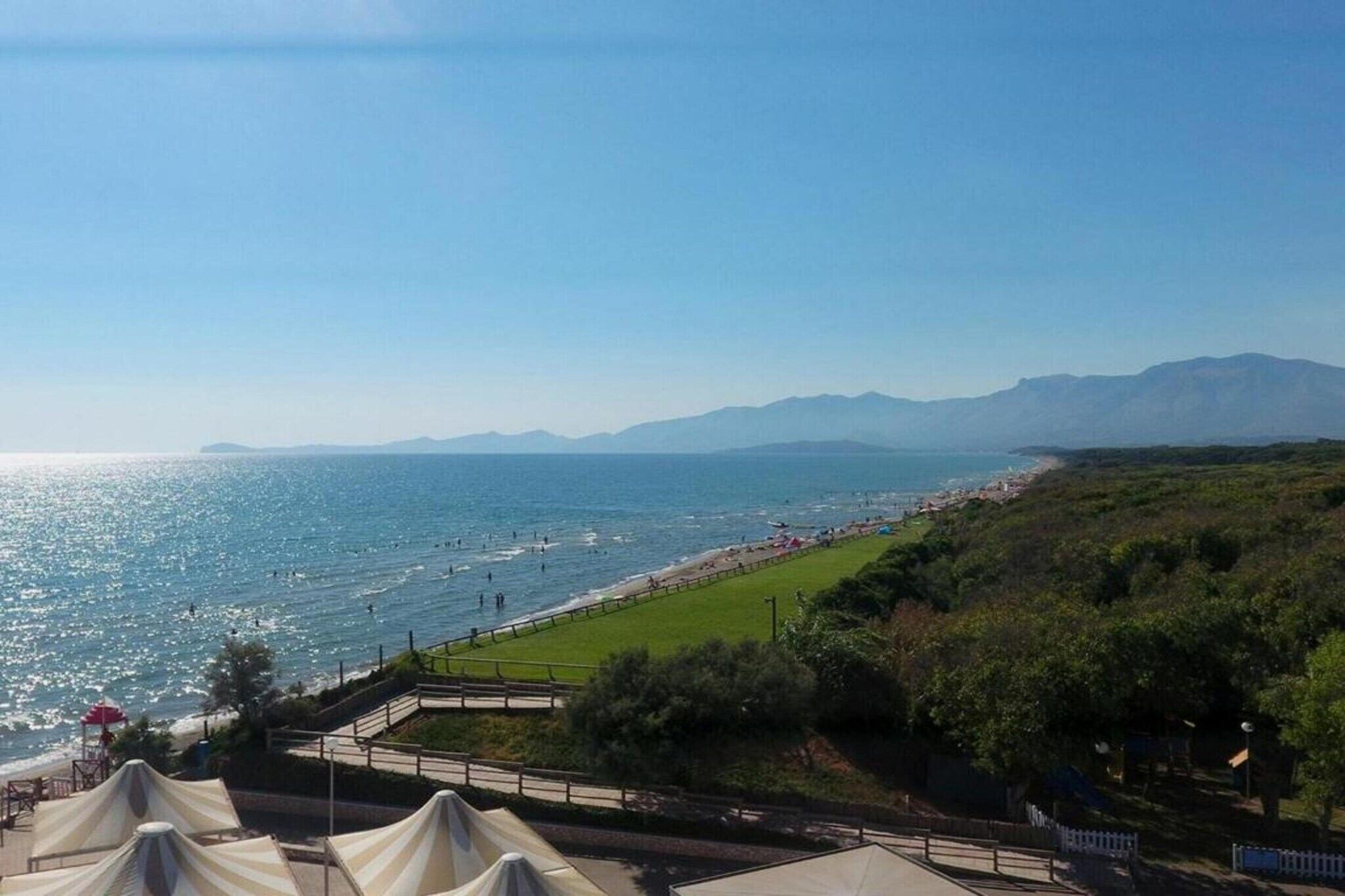 Eine Küstenansicht mit Strand, Grünflächen und Bergen im Hintergrund.