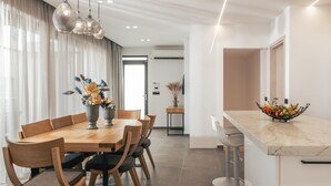Un comedor moderno con una mesa y sillas de madera, una encimera de mármol con frutero, e iluminación colgante.