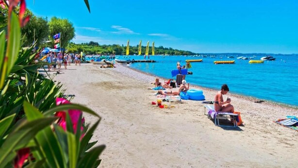 A beach with people sunbathing, boats in the water, and a clear sky. - Apartment in Lazise with Lake View & Pool (Lazise)
