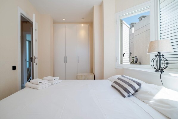 A bedroom with a bed, a window with blinds, a bedside lamp, and a wardrobe. - Holiday Home "House in first line of sea" with Garden, Terrace & Shared Pool (Sitges)
