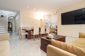 A modern living room with a dining area, a sofa, a coffee table, and a TV mounted on the wall.
