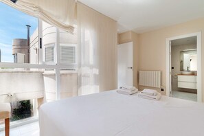 A bedroom with a large bed, a radiator, a bathroom with a sink and mirror, and a view of the outside.