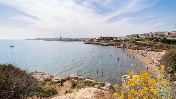 A coastal view with a beach, rocky shoreline, and buildings in the background.