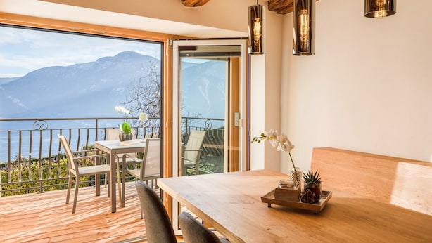 Un balcon avec une table et des chaises en bois, une plante en pot et une vue sur les montagnes.