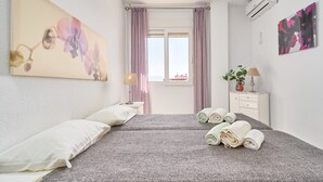 Une chambre d’hôtel comprenant un lit, des oreillers, une table de chevet avec une lampe, un climatiseur fixé au mur et une fenêtre avec des rideaux.