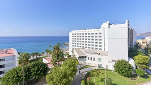 Un hôtel de grande hauteur offrant une vue sur l’océan, entouré de verdure et de palmiers.