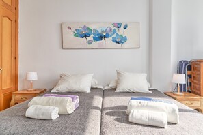 A double bed with white pillows, a bedside table with a lamp, and a painting of flowers on the wall.