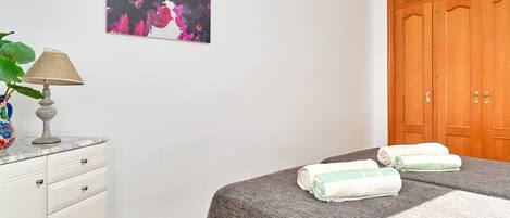 Un dormitorio con cama, armario de madera, escritorio con lámpara y un cuadro en la pared.