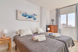 A hotel room with two beds, a painting on the wall, a wooden dresser, and a window with a view.