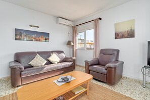 Een woonkamer met een bruine leren bank, een houten salontafel, een bruine lederen fauteuil, een tv-meubel en twee wandmontage airconditioners.