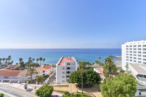 A coastal hotel with multiple floors, a red-tiled roof, and a view of the sea.
