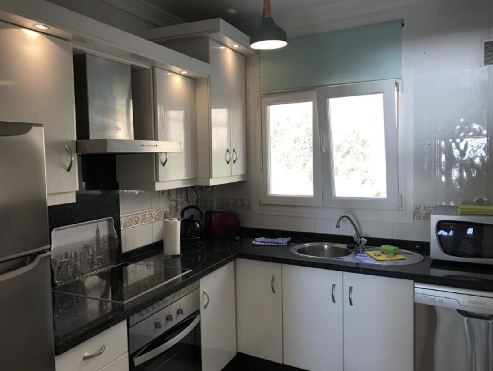 A kitchen with white cabinets, a black countertop, a stainless steel sink, and a window with daylight.