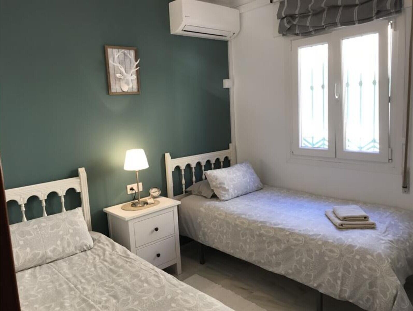 Una camera da letto con due letti, un comodino con una lampada, un condizionatore d'aria a muro e una finestra con vista.