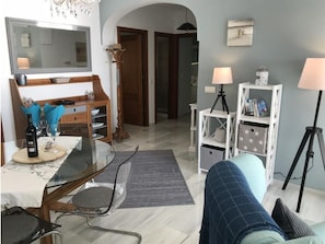 Een woonkamer met een glazen tafel, een bank, een lamp en een boekenkast.