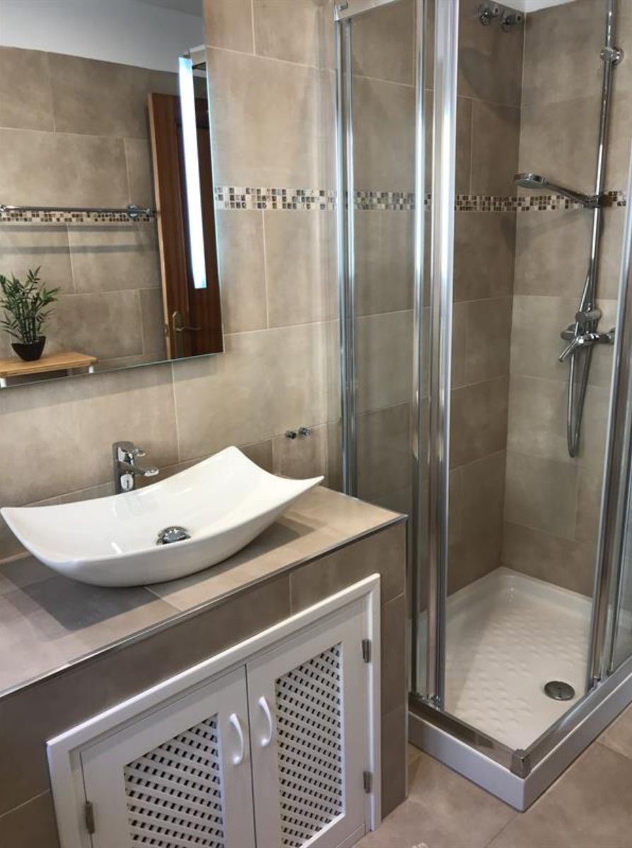 Un bagno moderno con un lavabo a incasso, cabina doccia in vetro e mobiletto con specchio.