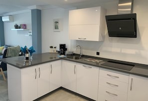 Une cuisine moderne avec des meubles blancs, un plan de travail noir, une machine à café et un four à micro-ondes encastré.